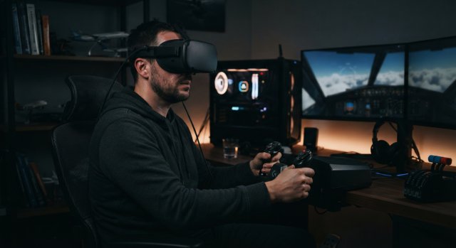 Ein Nutzer in einem Flugsimulator-Cockpit mit einer VR-Brille vor einem PC-Setup mit drei Monitoren.