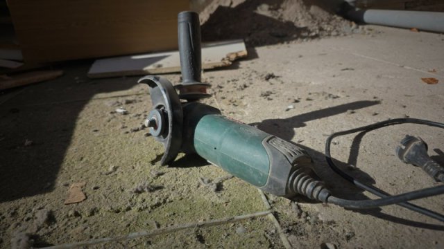 Gr&uuml;ner Bosch-Winkelschleifer ohne Trennscheibe auf staubigem Baustellenboden mit Stromkabel.